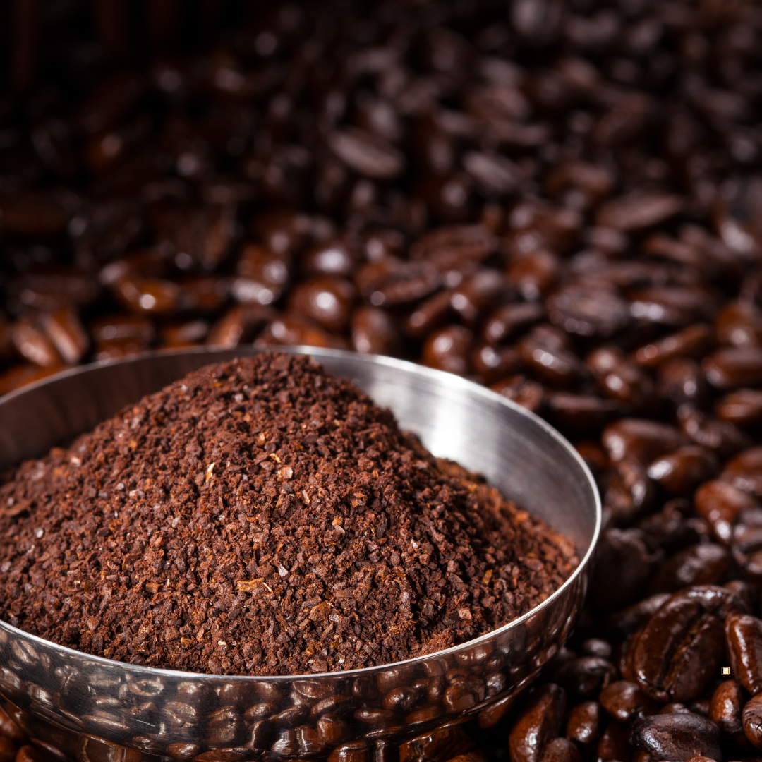 decaf ground coffee in a stainless steel cup surrounded by whole bean decaf coffee beans