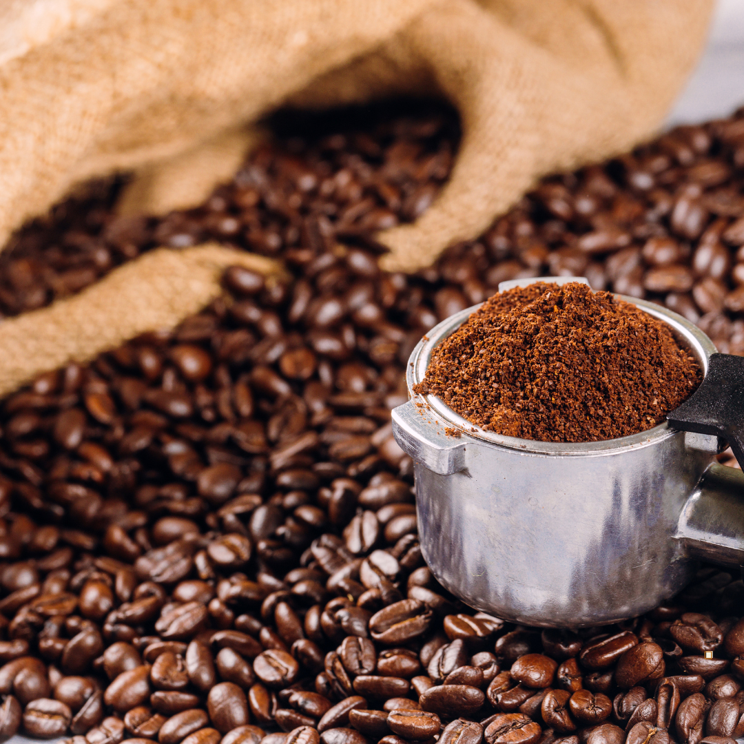 ground small batch coffee in a metal scoop surrounded by coffee beans
